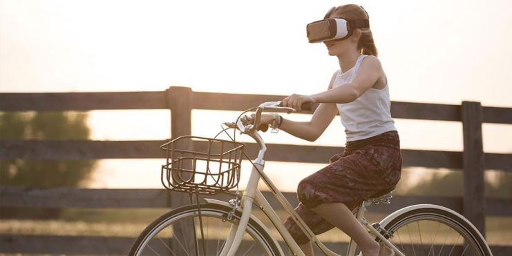 Ein Mensch fährt auf einem Fahrrad durch die Natur und trägt dabei eine VR Brille